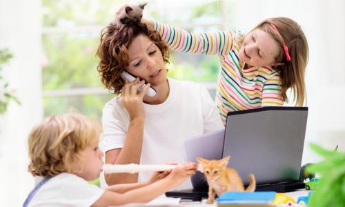 mother working from home on laptop and phone with two young children and kittens playing around her