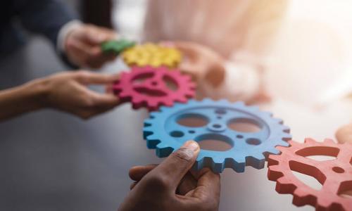 hands holding together many different colored cogwheels and gears