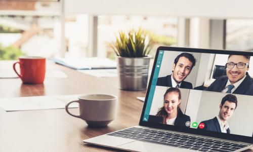 hybrid meeting with coffee mugs and a laptop with executives in a video session on a table