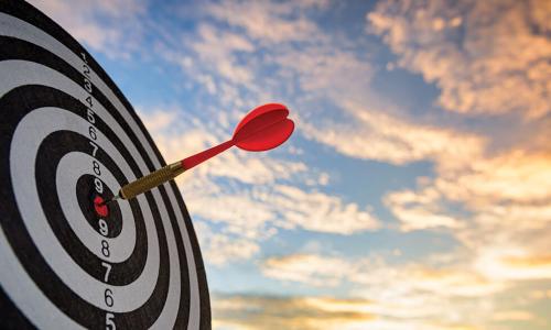 red dart in bullseye of a target against a cloudy sunset sky