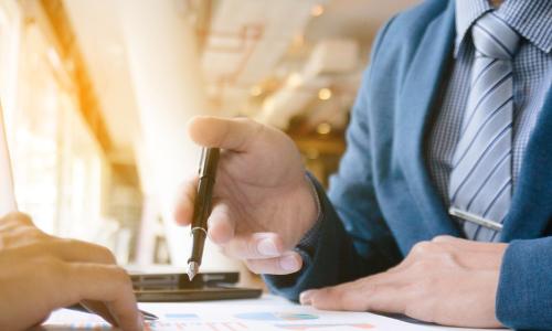 businessman in tie holding pen and gesturing to a report while colleague reviews