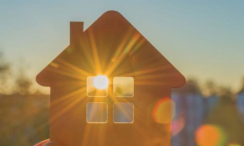 Hand holding up a wooden cutout of a house to let the sun shine through the windows