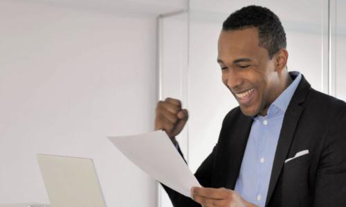 businessman celebrating with fist, laptop, paper