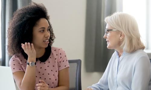 older white woman mentors younger Black woman at the office