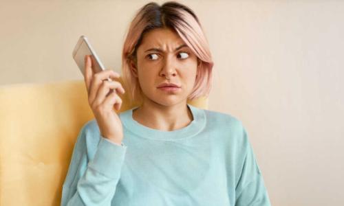 Portrait of frowning young woman in blue sweatshirt holding mobile phone