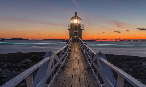 lighthouse shining in front of cloudy sunset sky