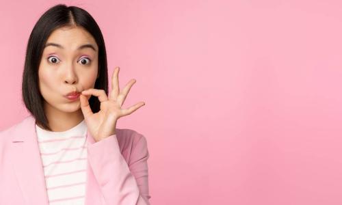 young Asian businesswoman in pink suit pinching lips shut to keep a secret