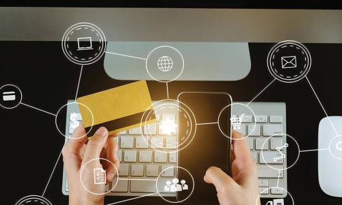 person in yellow sweater using credit card and smartphone in front of computer with icons representing ecommerce 