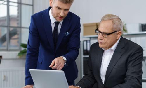 mature executive and young executive work on laptop in office