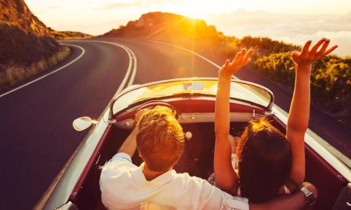 raised arms while driving car at sunset