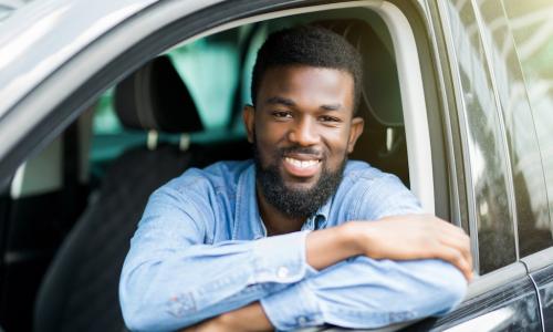 smiling young man sitting inside and leaning through open window of new car