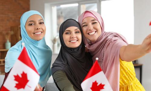 three young Muslim women in colorful headscarves wave Canadian flag