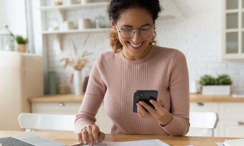 woman files at offer on smartphone while working on financial statements on calculator and laptop