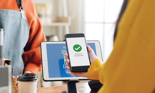 woman in yellow sweater uses mobile tap-to-pay at a café